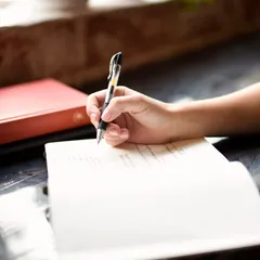 Une main qui écrit sur une feuille, près d'une fenêtre