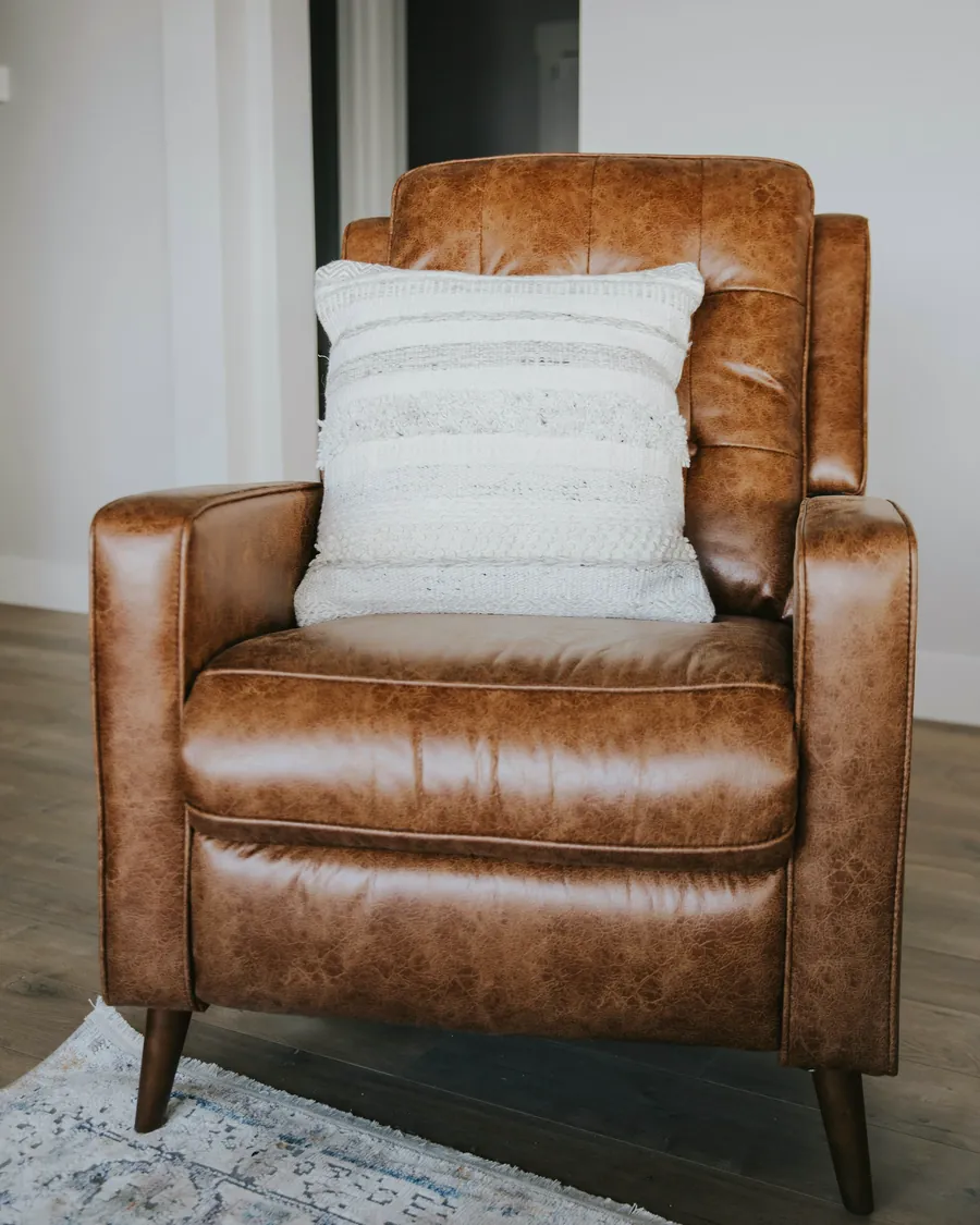 Un fauteuil en cuir brun garni d'un coussin clair, devant un mur gris