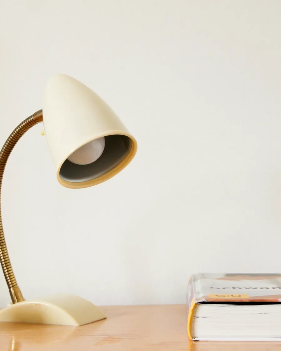 Une lampe de bureau crème allumée près d'une pile de livres sur une table en bois