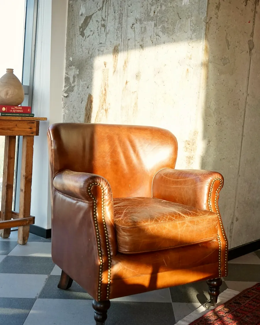 Un fauteuil en cuir orangé près d'une grande fenêtre, dans une pièce lumineuse