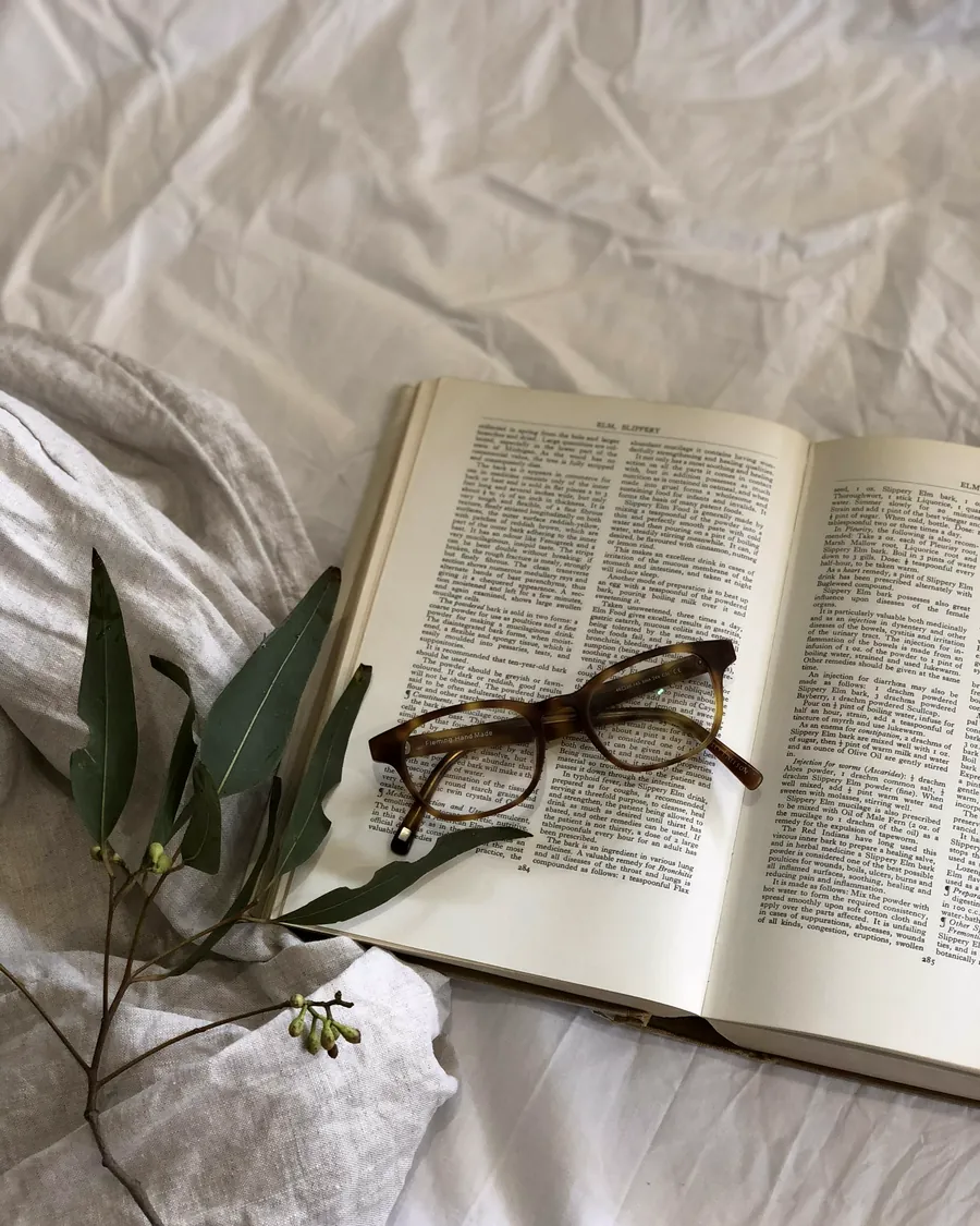 Une paire de lunettes posée sur les pages ouvertes d'un livre, sur un drap froissé