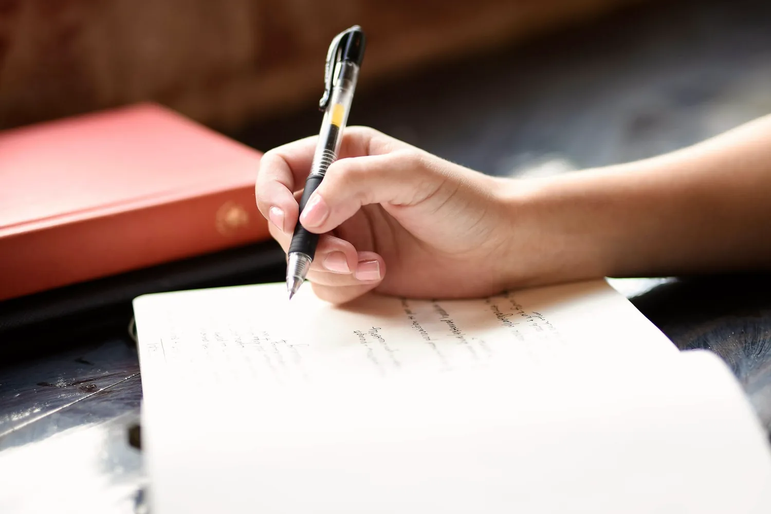 Une main qui écrit à la plume sur une feuille près d'une fenêtre