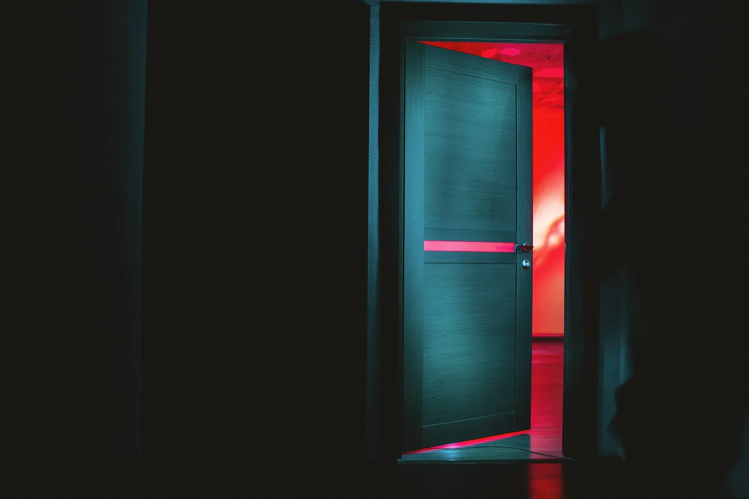 Une porte entrouverte dans un couloir sombre, avec une lumière rouge derrière
